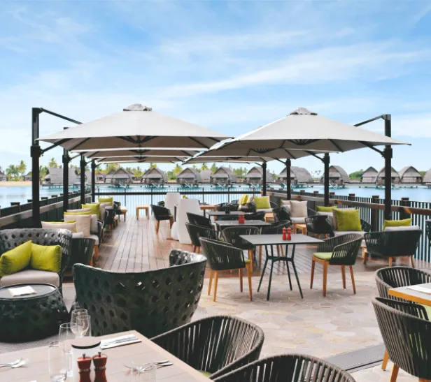 Resort-style outdoor dining area with large commercial umbrellas providing shade over multiple seating arrangements